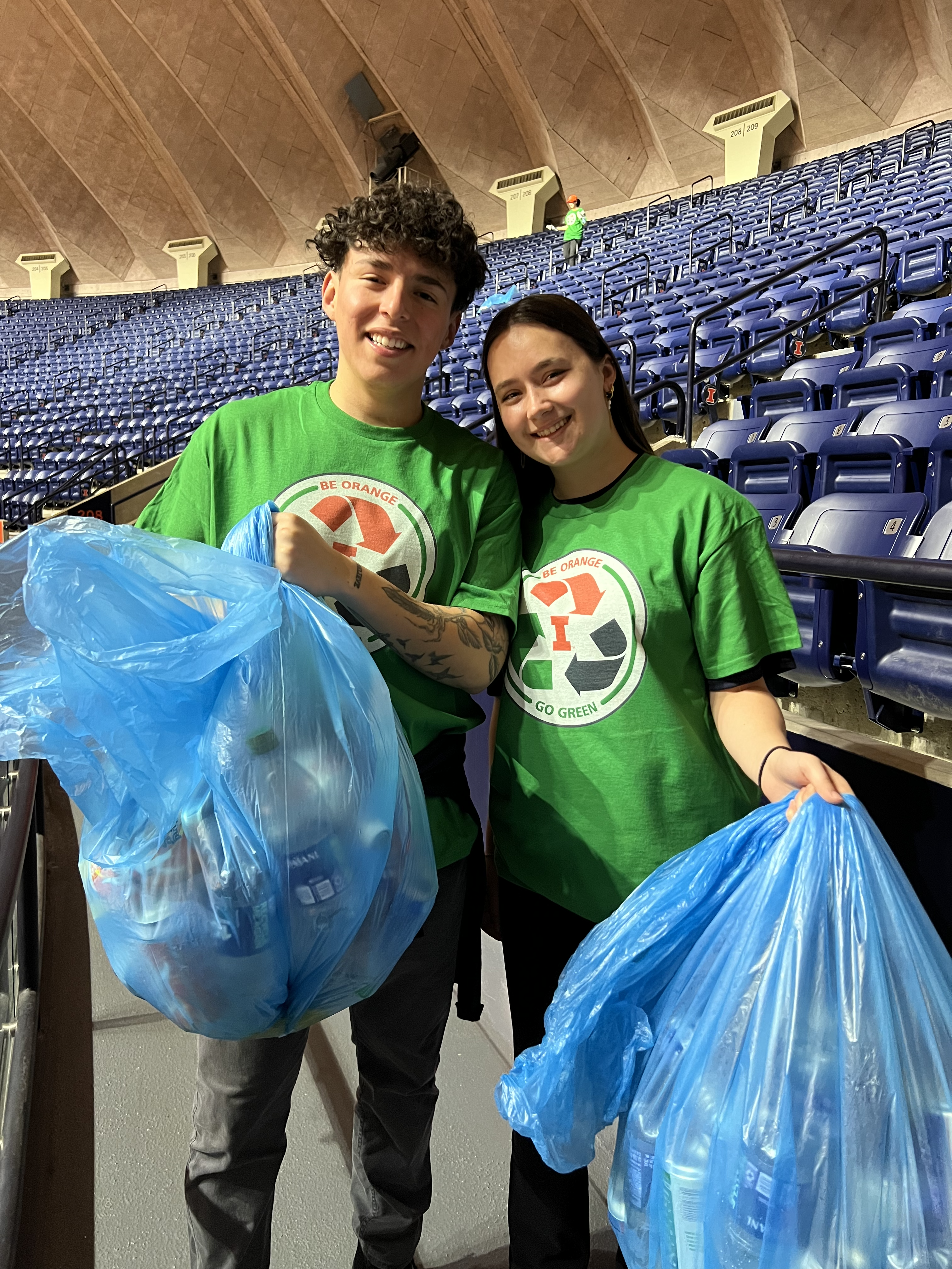 Two F&S volunteer's holding bags of recycling in the stadium.