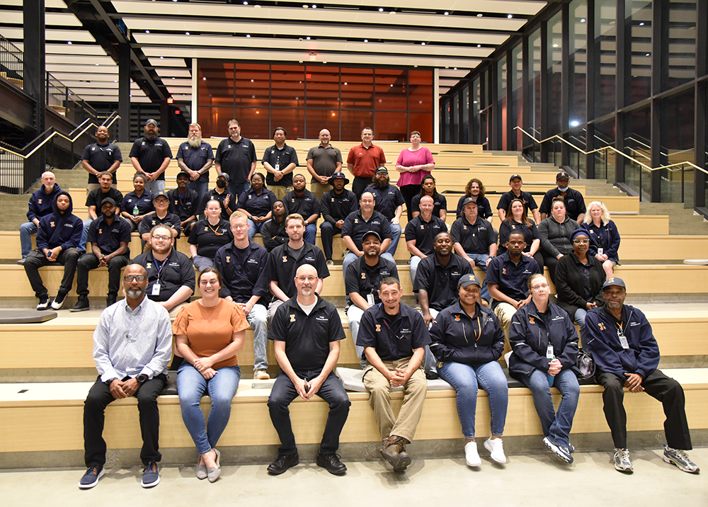Approximately 30 F&S Building Services staff pose for a group picture on the studying area of the Campus Instructional Facility with theatre-type seating