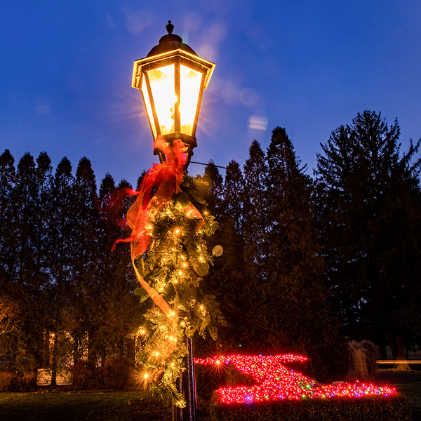 A light pole decorated with garland and lights for the holidays. An orange Block I is lit up in the background as well.