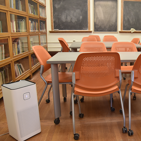 Air purifier located in a classroom by a desk with several orange chairs