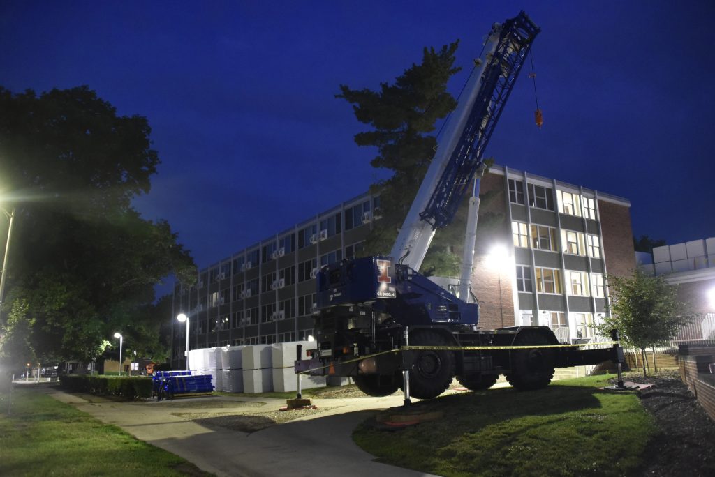 A crane truck sits outside of the Pennsylvania Avenue Residence Hall at night with construction materials in the background.