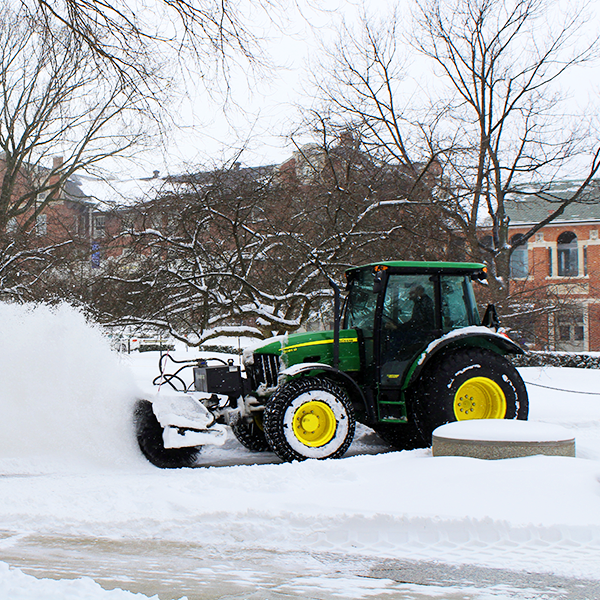 A John Deere tractor moving snow and ice from a campus pathway.