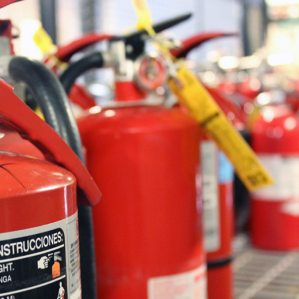 Red fire extinguishers sit on a shelf. One of the extinguishers displays a yellow tag on its valve.