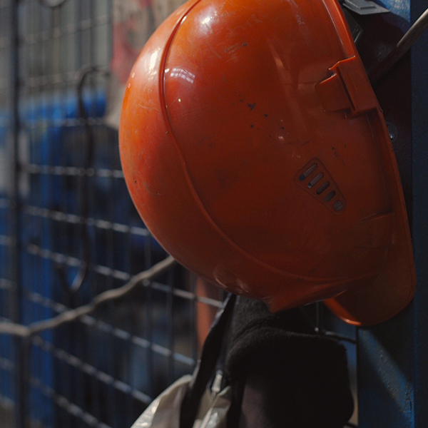 An orange hard hat hangs on a chain link fence.