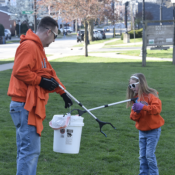 An adult and a kid use grabbers to place trash into a collection at Boneyard Creek Community Day.